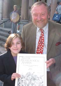 Shows a photo of Francis Pryor, wearing a suit and red patterned tie, with Beth next to him in a dark top. They're both grinning and holding a certificate.