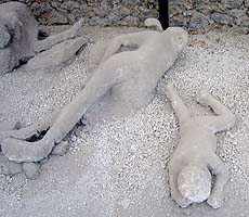 Photo showing bodies from Pompeii including an adult and child. The bodies are covered in ash and lying on the ground.