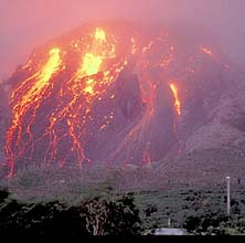 Evening photo of a volcano with a lava dome showing and lava pouring down the side of the volcano.