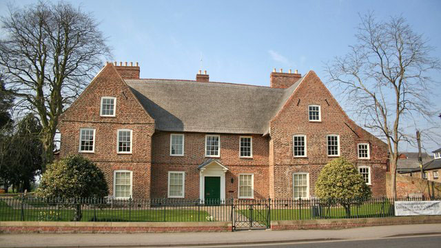 Image of a red brick manor house with a thatched roof.