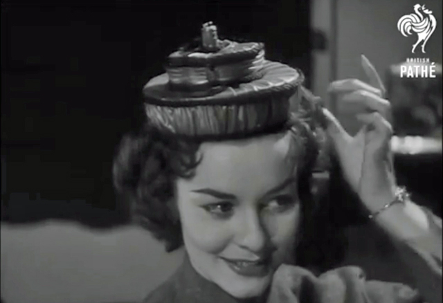 A black and white screenshot showing a woman in an unusual hat