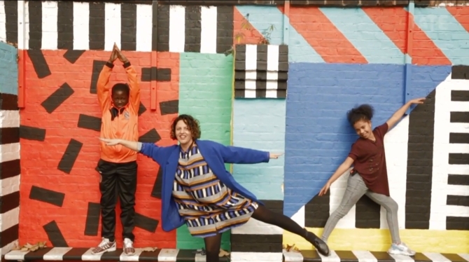 3 people pose in front of a colourfully painted wall.