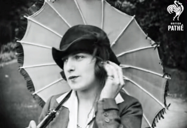 A black and white screenshot showing a woman with a portable music player holding an umbrella