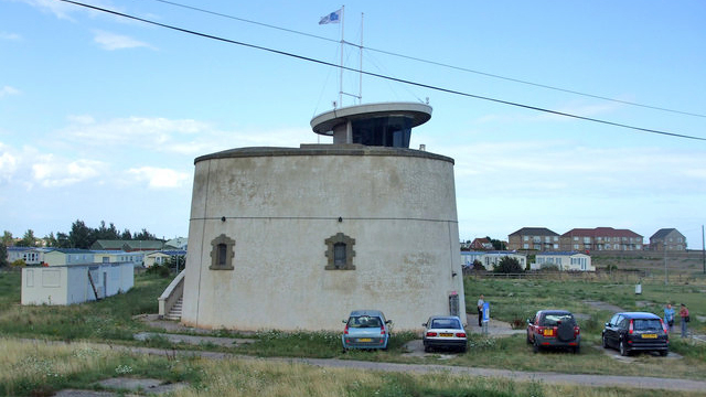 A grey round Martello tower with cars parked outside of it