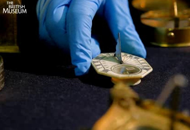 A blue gloved hand holding a sundial. 