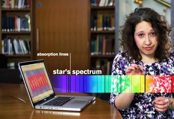 A screenshot showing a woman and a laptop in a library, she is explaing light spectrum.