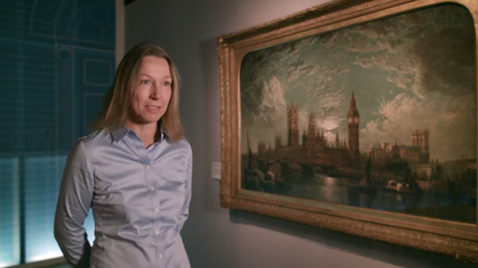 A screenshot showing a woman standing in front of a painting of the Houses of Parliament