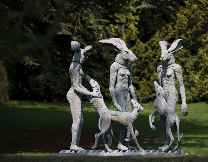 A photograph of a statue of three figures in a garden